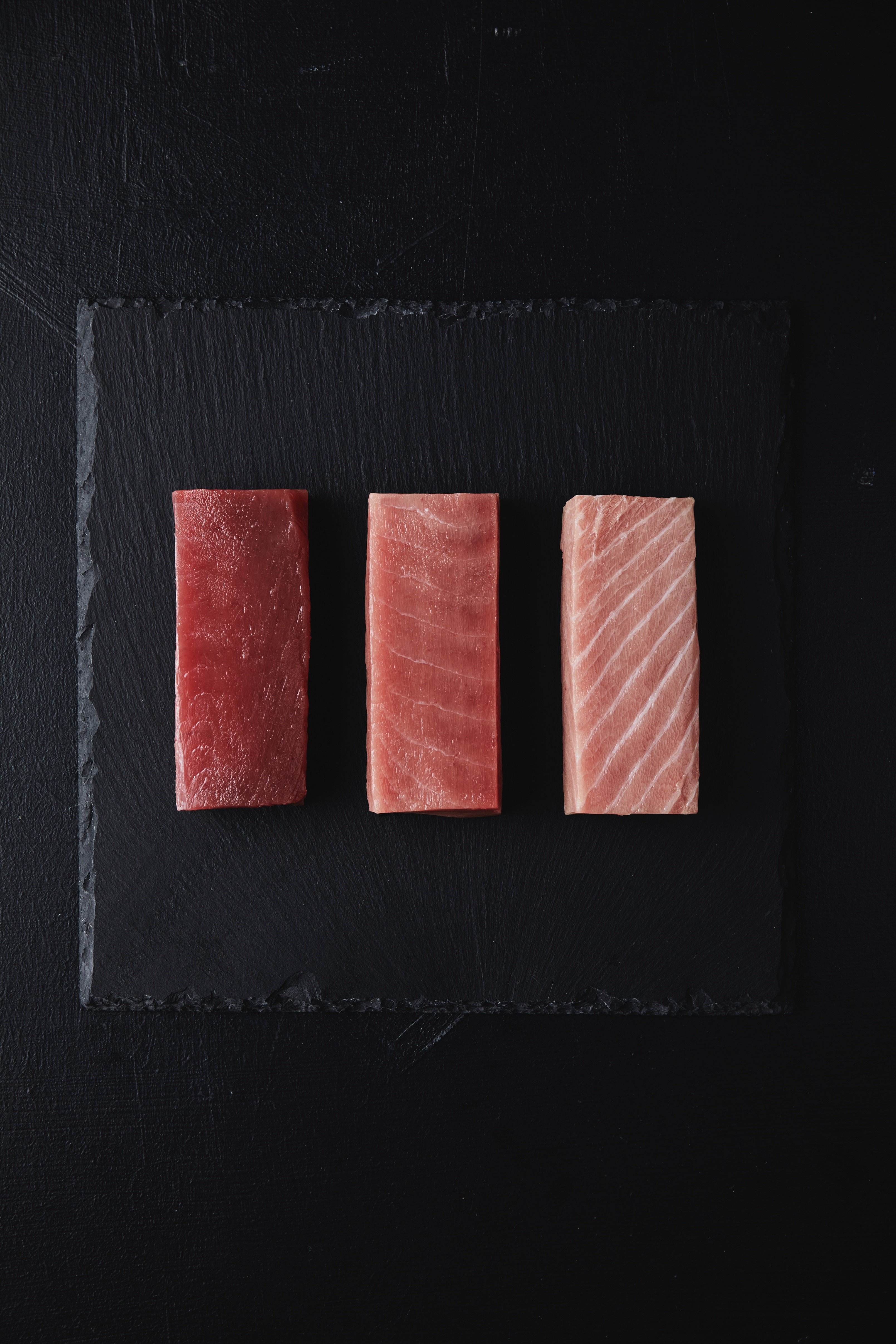 Three cuts of tuna presented on black cutting board