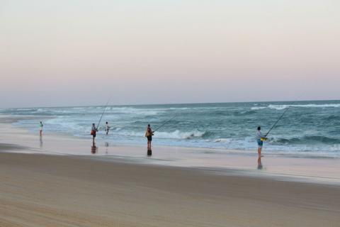 Photo of a beach at sunset with people fishing